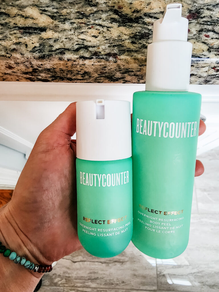 close up of hand holding teal bottles of beautycounter overnight resurfacing peel for face and body; reflect effect overnight resurfacing peel results